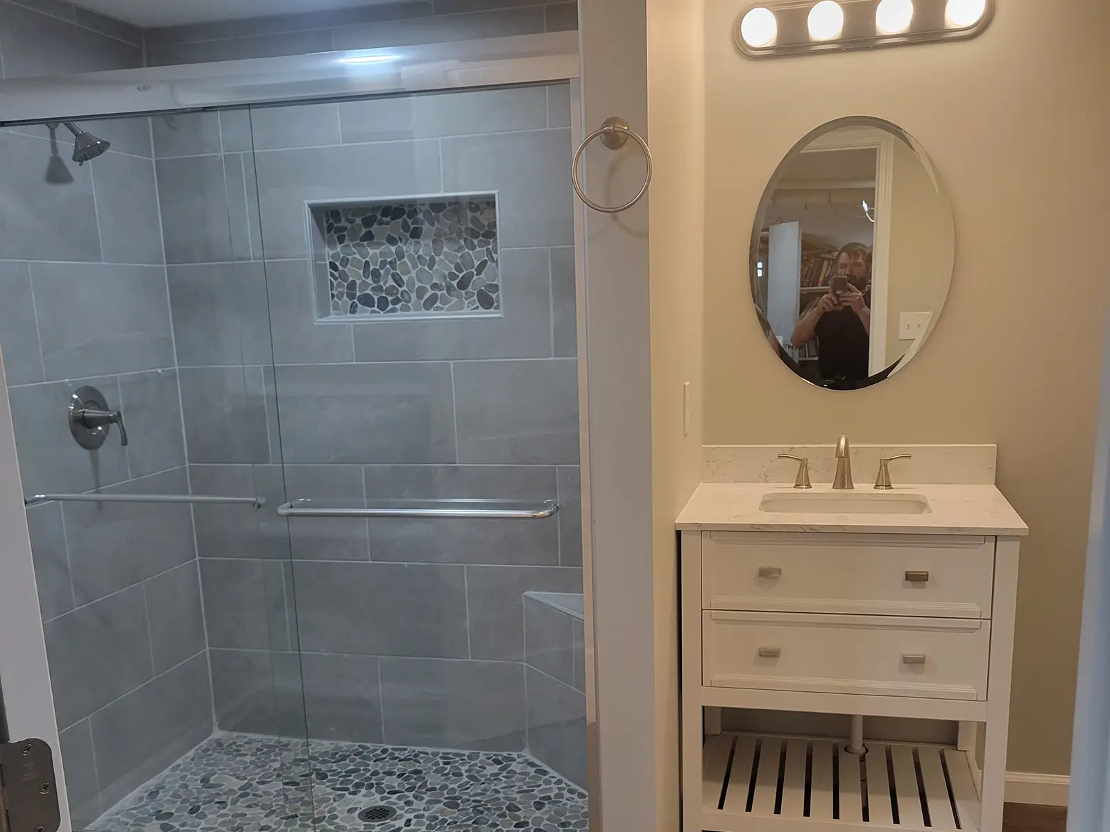 Bathroom remodel with walk-in tile shower, pebble-stone accents, frameless glass, and a white vanity.