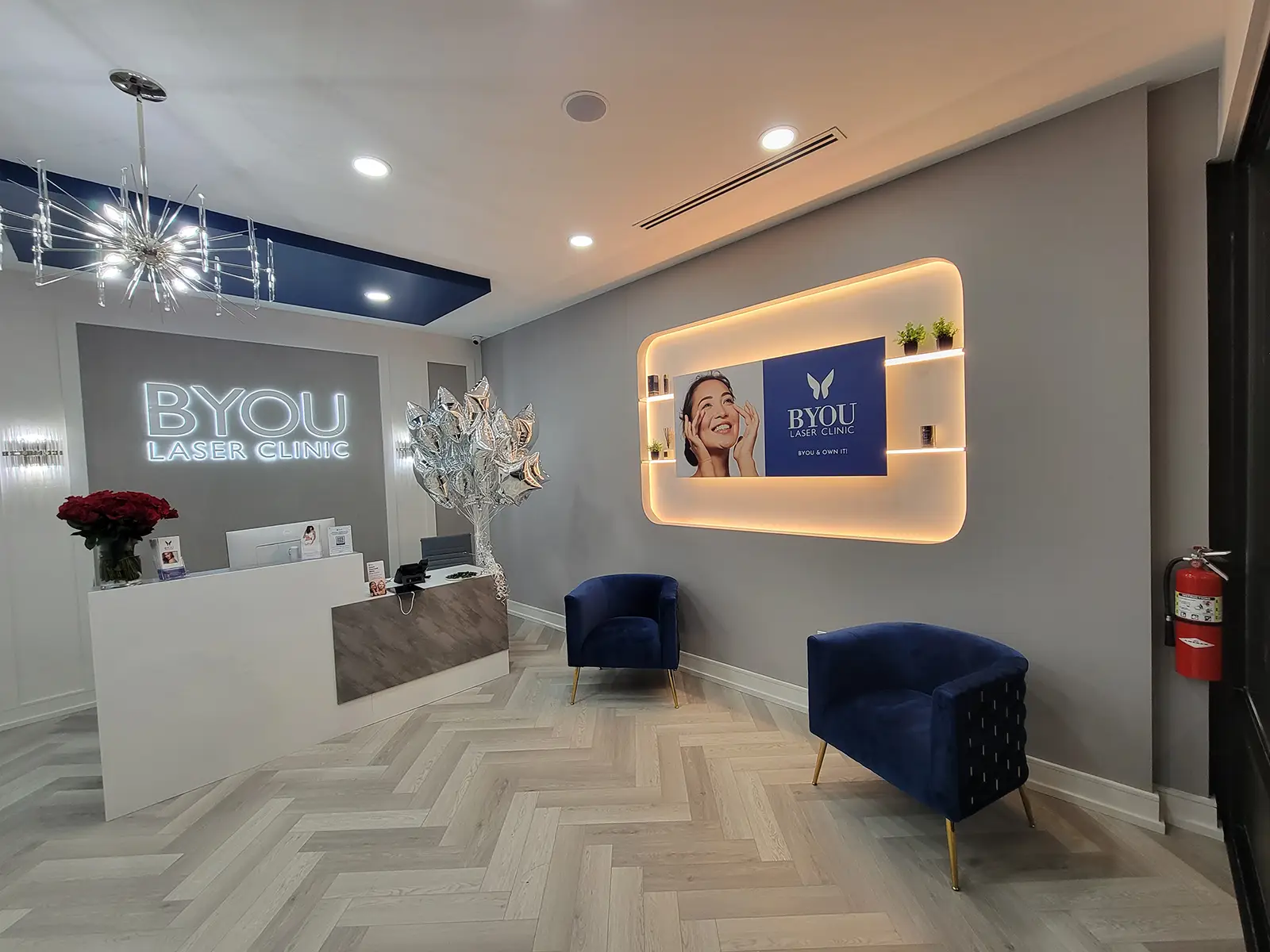 Commercial clinic lobby build-out with reception desk, herringbone floors, backlit display shelving, and modern lighting.