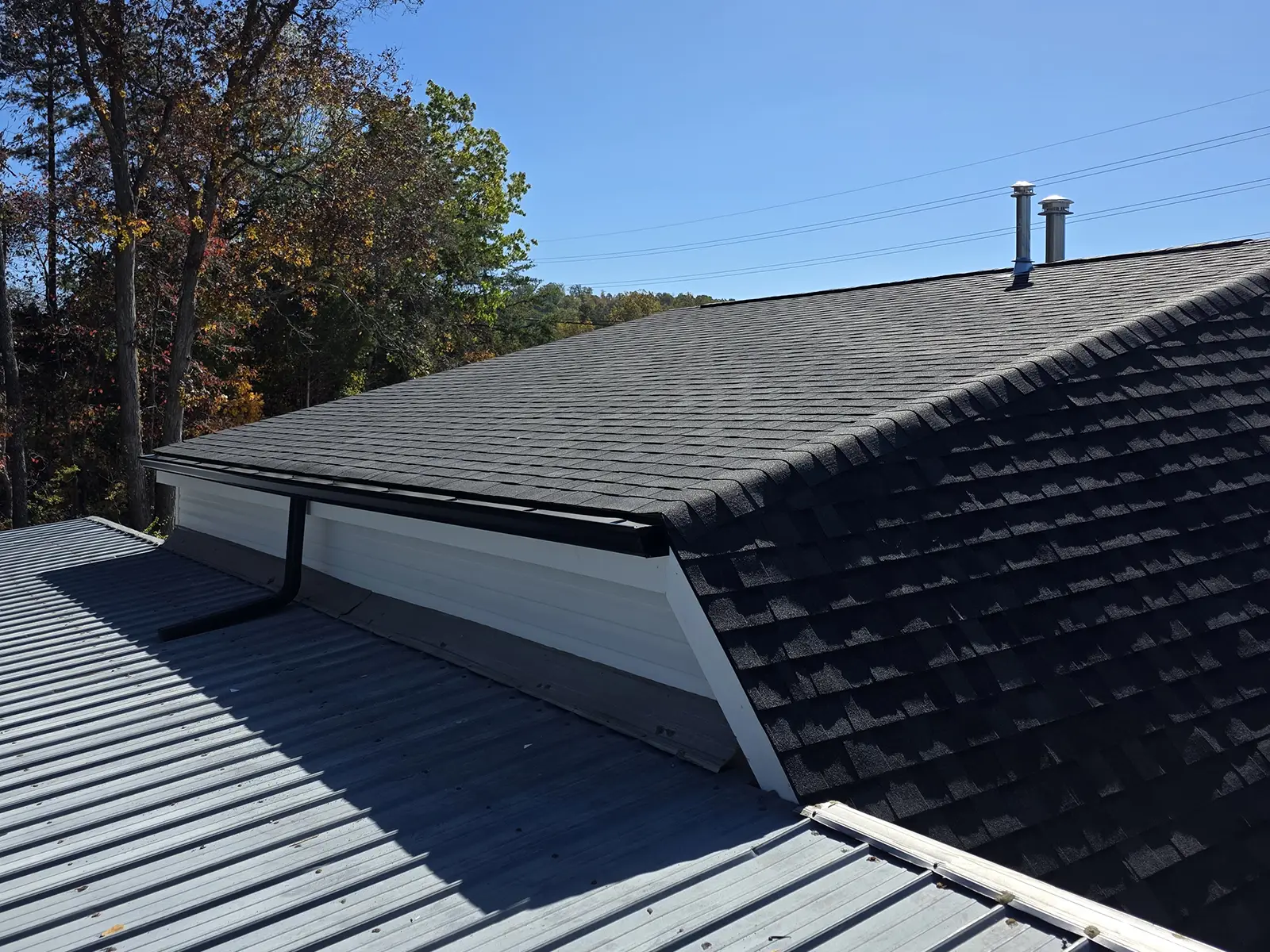 Roof raised for commercial auto-shop using architectural shingles tied into an existing metal roof with drip edge and vent stacks visible.