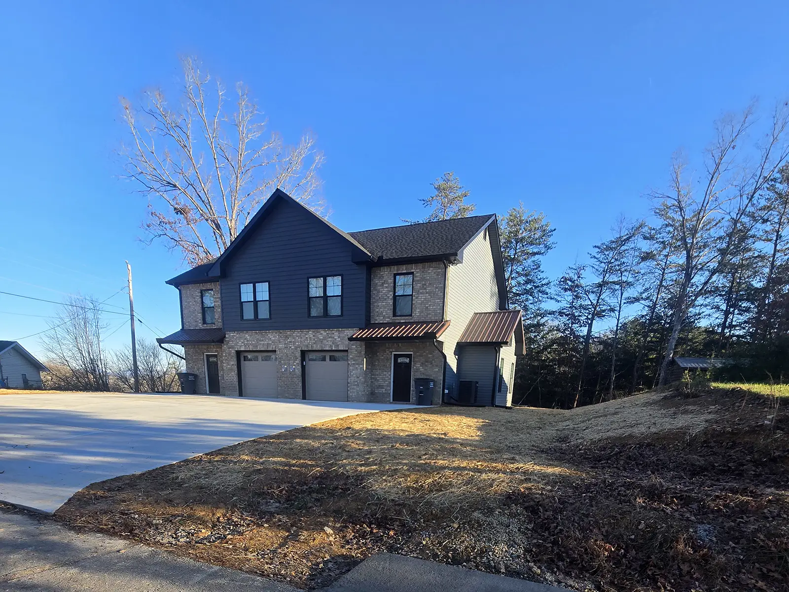 New-construction duplex featuring brick and board-and-batten siding, metal awnings, and a wide concrete driveway.