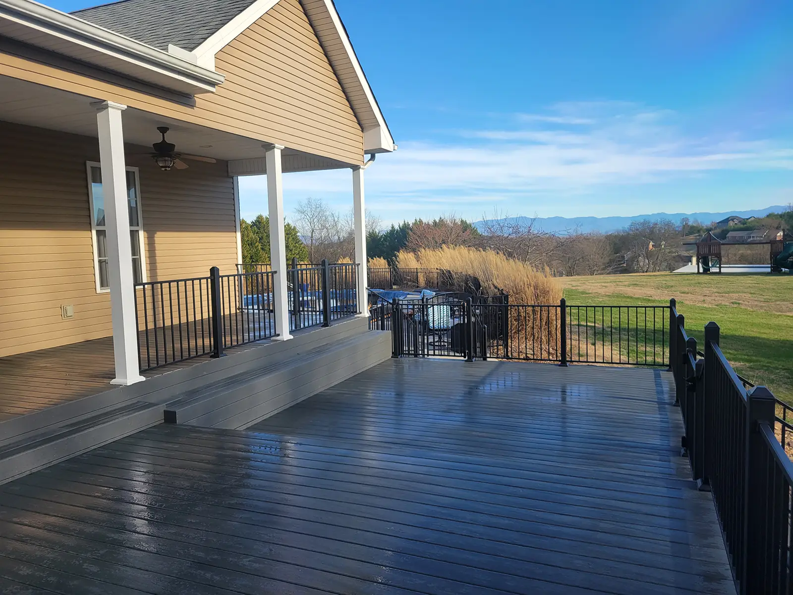 Large composite deck addition with black aluminum railing, tied into a covered porch overlooking open views.