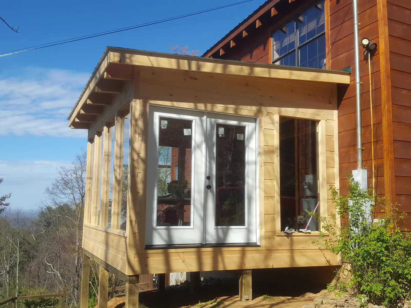 Sunroom addition with wood framing, French doors, and tall windows on a pier foundation attached to the home.